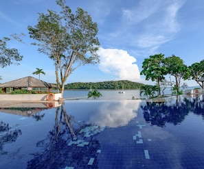 A clear view of a swimming pool with a tiled floor, surrounded by trees and a body of water in the background.