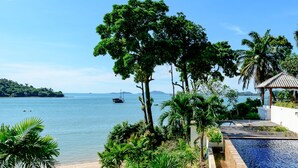 A poolside view with a beach, palm trees, and a distant boat on the water. - Chandara Resort & Spa Phuket (Pa Klok)