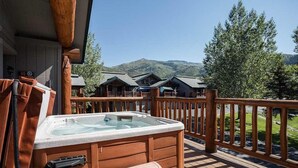 Une terrasse en bois avec un jacuzzi, des bancs en bois et une vue sur des chalets en arrière-plan.