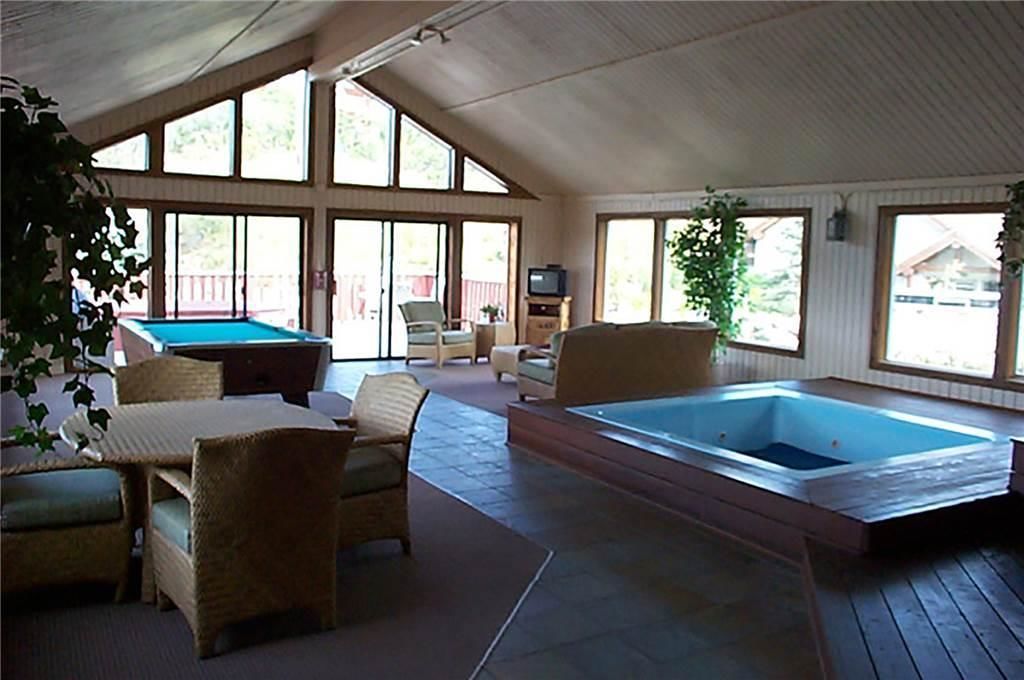 A spacious indoor area with a pool table, lounge chairs, and a hot tub.