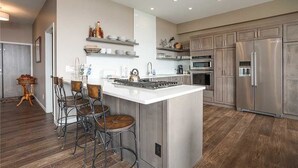 Une cuisine moderne dotée d’un îlot central, de tabourets de bar, d’appareils électroménagers en acier inoxydable et d’un revêtement de sol en bois.
