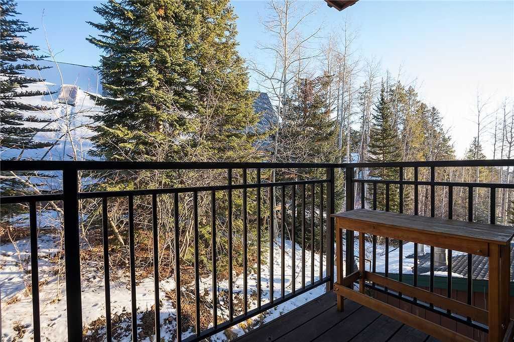 Una terraza de madera con barandilla metálica, con vista a un paisaje nevado con árboles y una montaña al fondo.