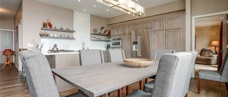 A modern kitchen with a dining area, featuring a large wooden table, grey upholstered chairs, and built-in cabinets.