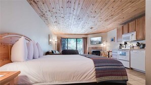 Une chambre avec un grand lit, un plafond en bois et une kitchenette équipée d’un four à micro-ondes et d’une cuisinière.