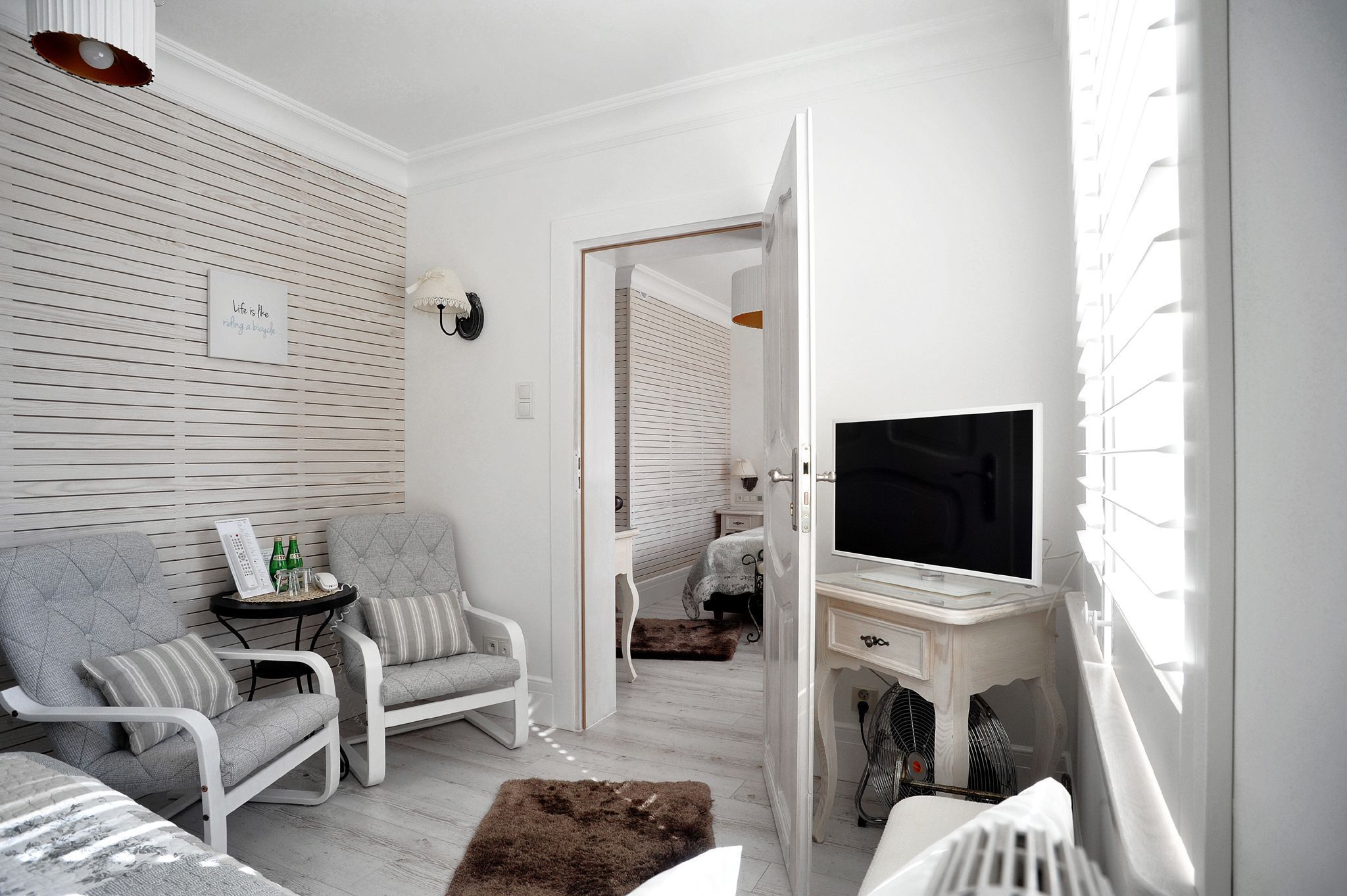 Una sala de estar moderna con un sofá, una mesita con botellas, un televisor y un escritorio blanco.