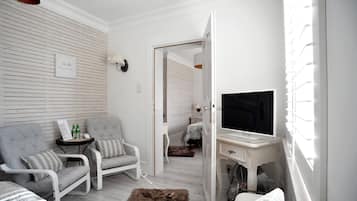 Una sala de estar moderna con un sofá, una mesita con botellas, un televisor y un escritorio blanco.