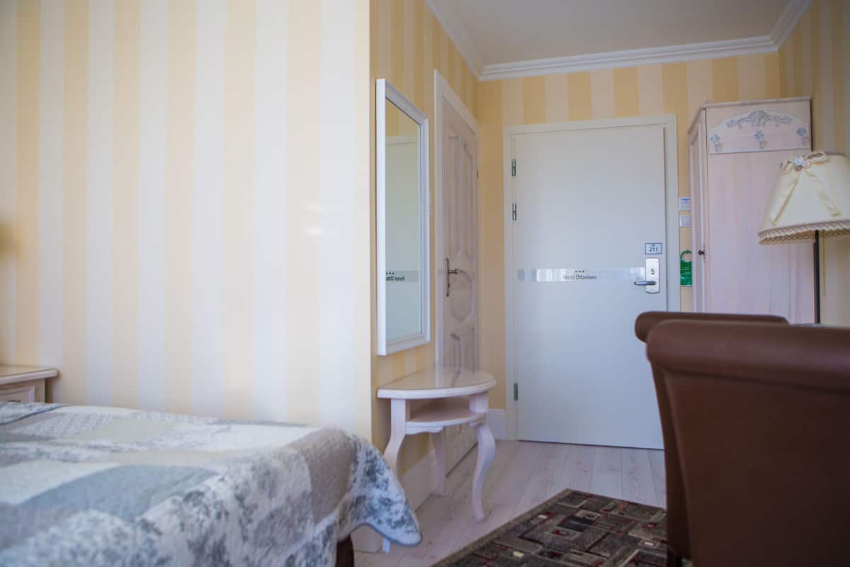 Hotellihuone, jossa on sänky, pieni pöytä, tuoli, ovi ja lamppu.