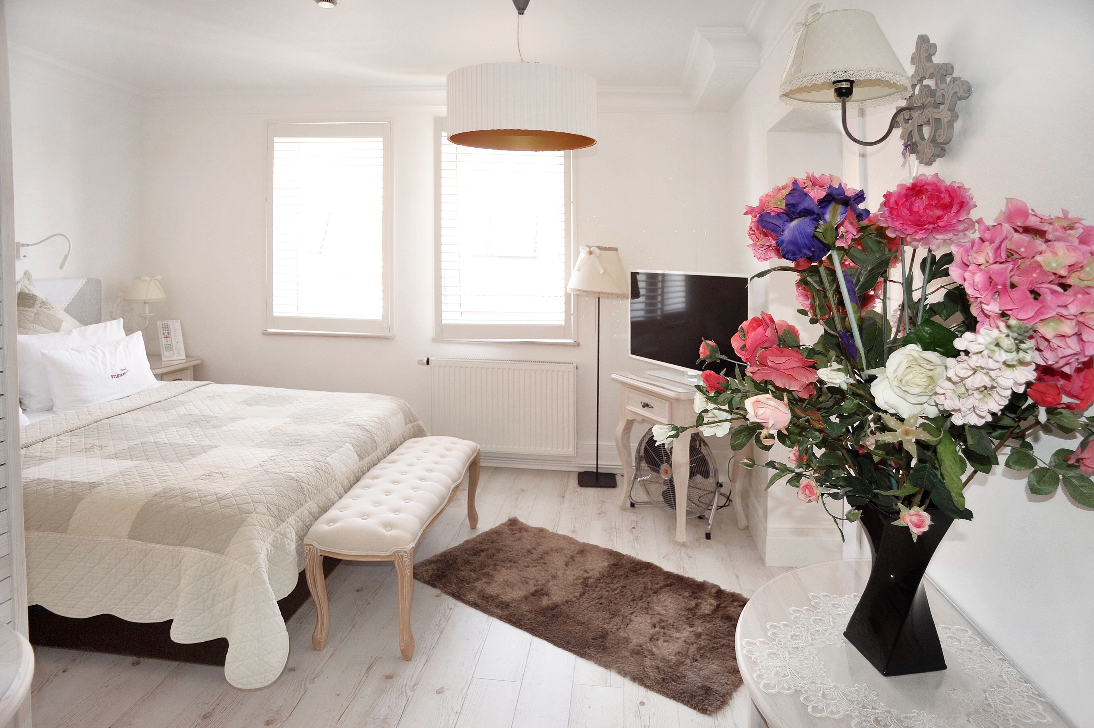 A bedroom with a bed, bedside table, TV, and a large floral arrangement.