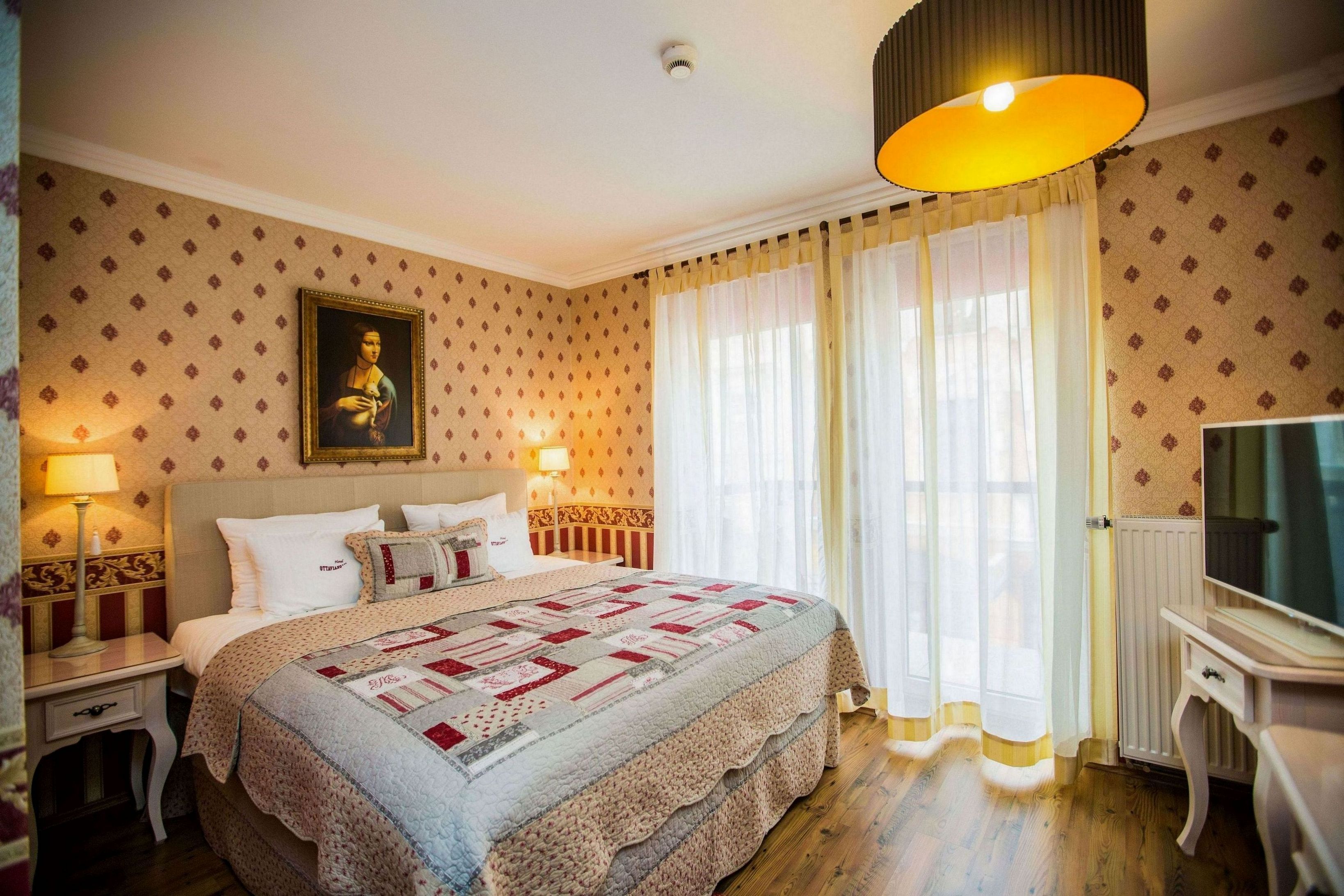 A hotel room with a large bed, a television, a nightstand, and a lamp.