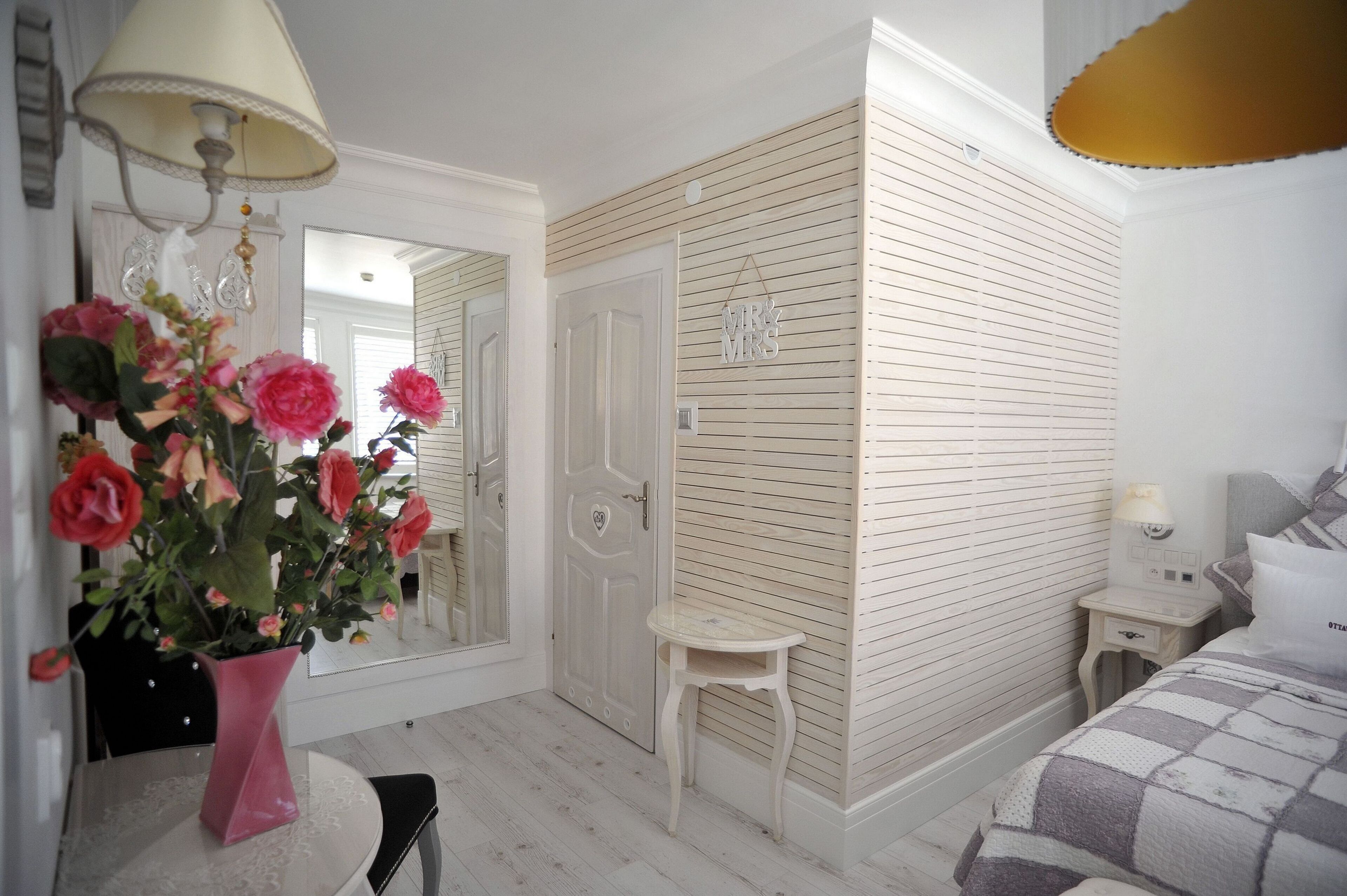 A bedroom with a bed, bedside table, lamp, and a mirror.