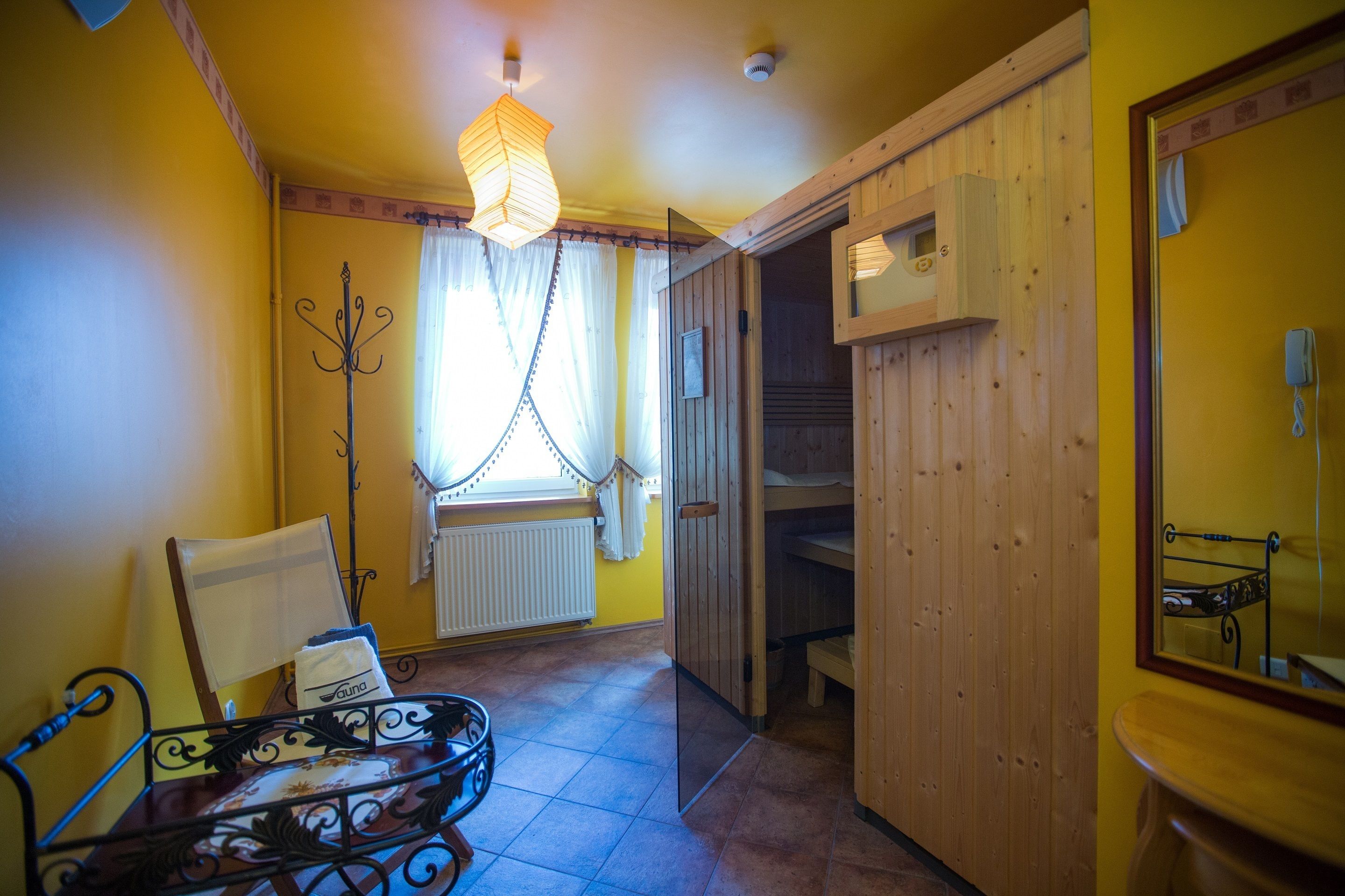 Una habitación con cama, una silla, una mesa, ventana con cortinas, radiador y armario de madera.