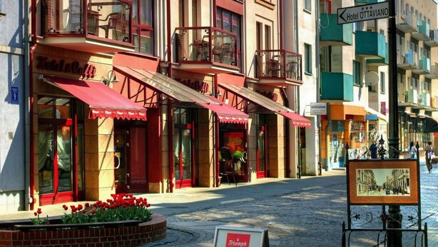 Un hotel con varios pisos, balcones y un toldo rojo.