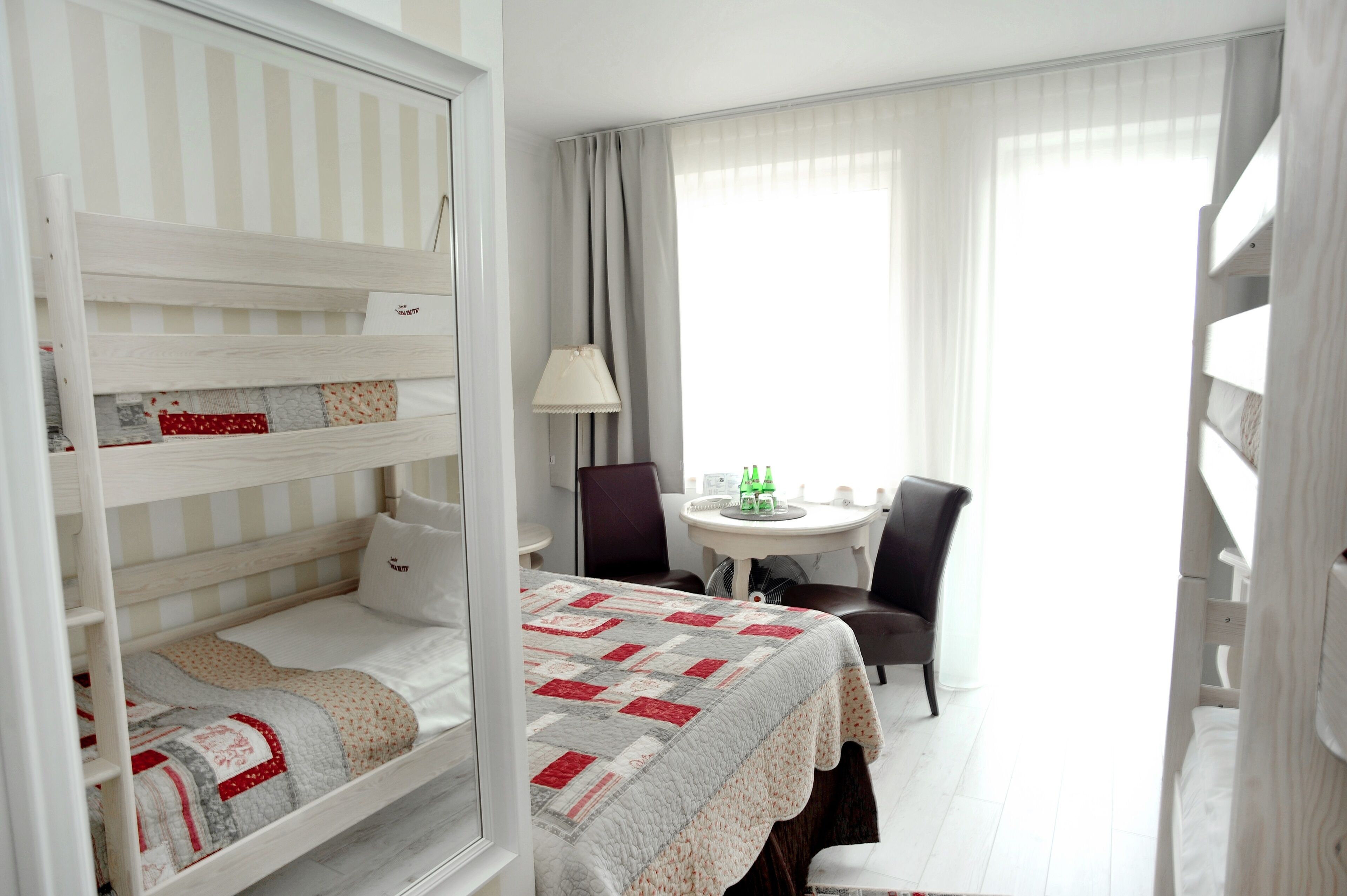 Una camera d'albergo con un letto a castello, un piccolo tavolo rotondo con sedie e una finestra con tende.