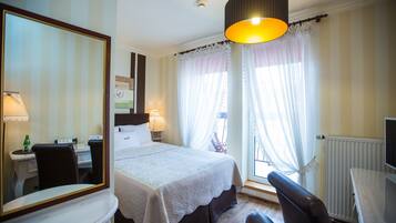 Habitación de hotel con cama, escritorio, silla, espejo y ventana con cortinas.