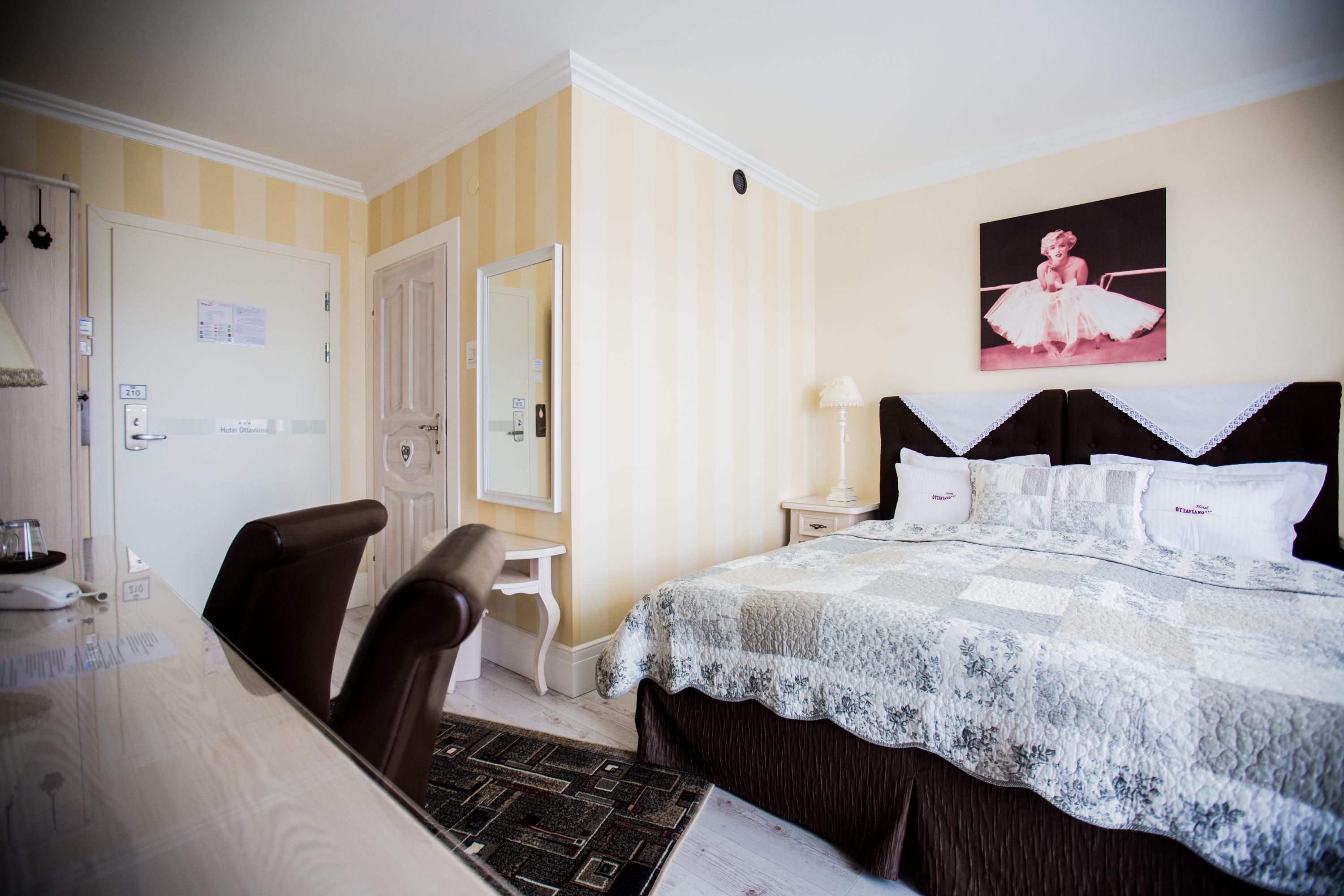 Une chambre d’hôtel comprenant un lit, un bureau, une chaise, une table de chevet et un tableau accroché au mur.