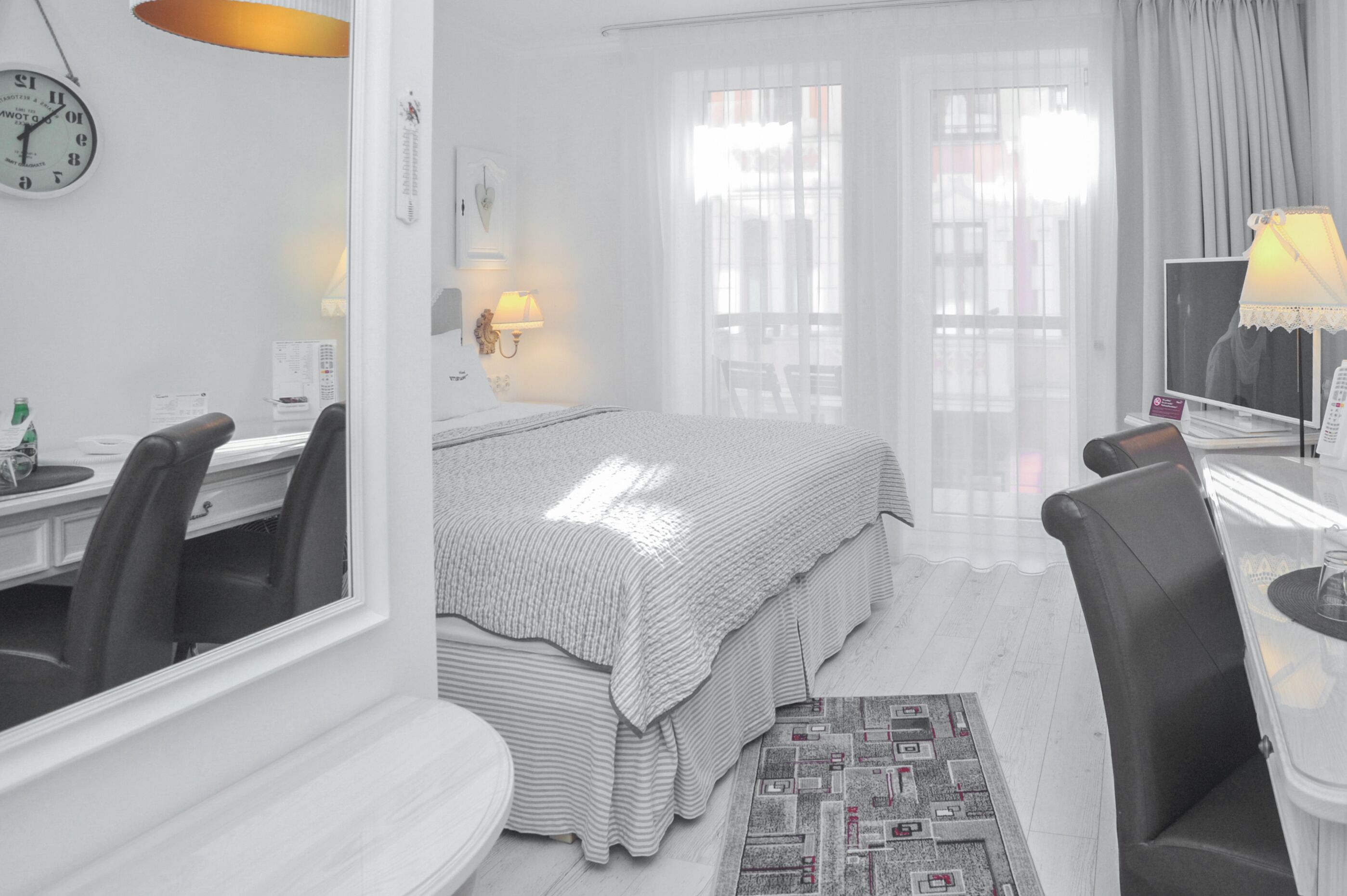 A hotel room with a bed, a desk with a chair, a television, and a window with curtains.
