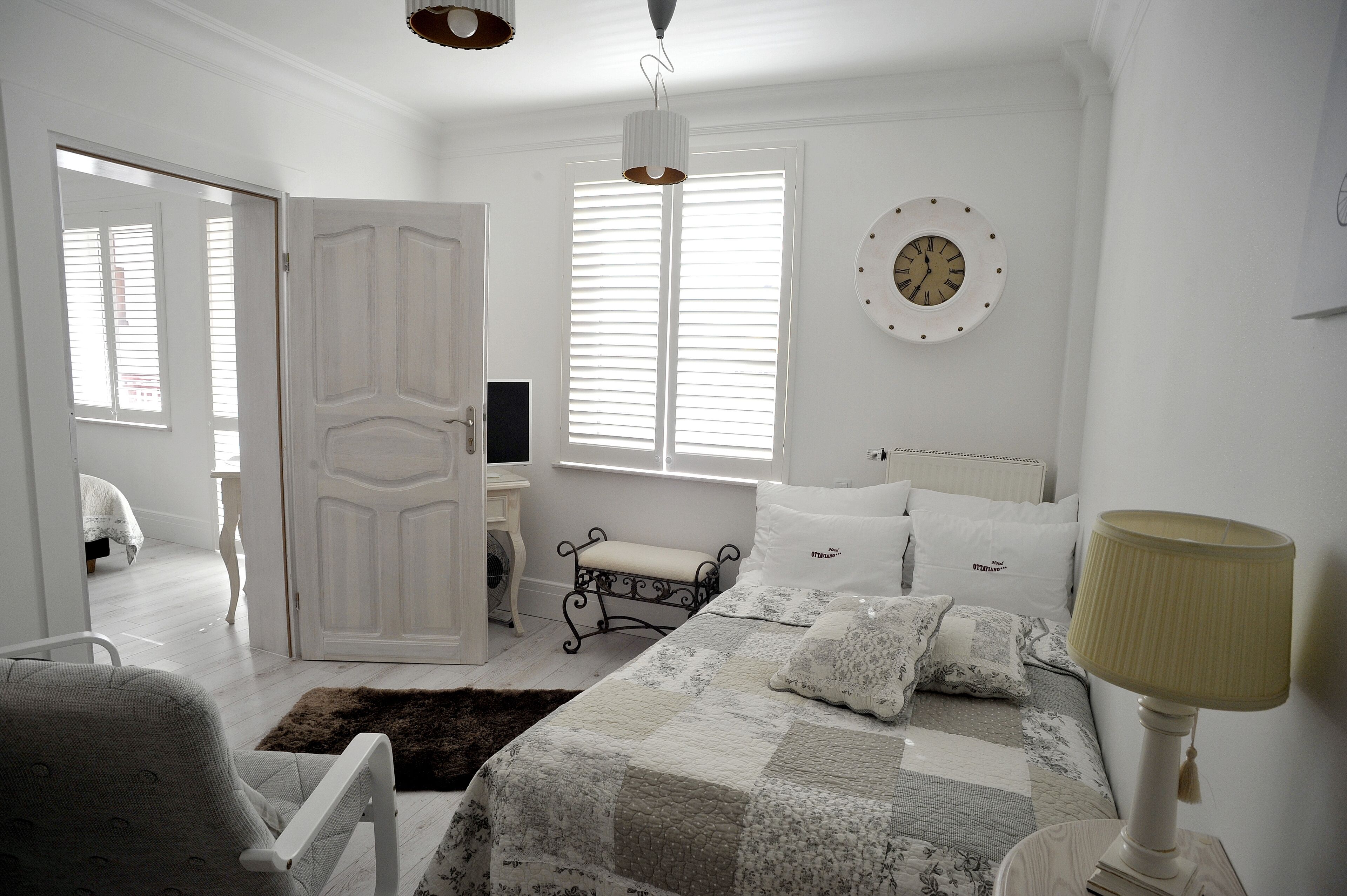 A bedroom with a bed, bedside table, lamp, and a clock on the wall.