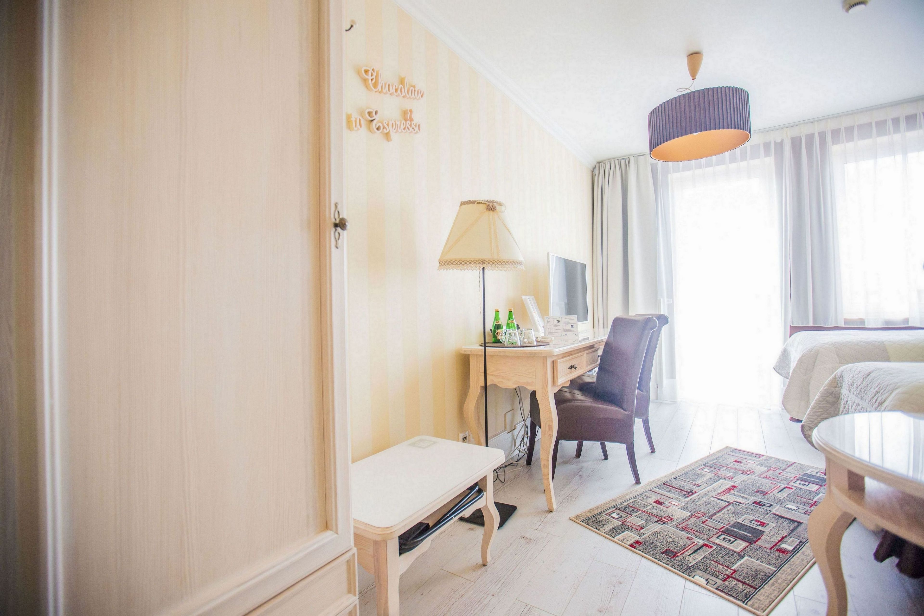 A hotel room with a bed, a desk with a lamp, a chair, a small table, and a rug.