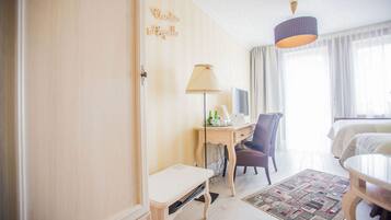 A hotel room with a bed, a desk with a lamp, a chair, a small table, and a rug.