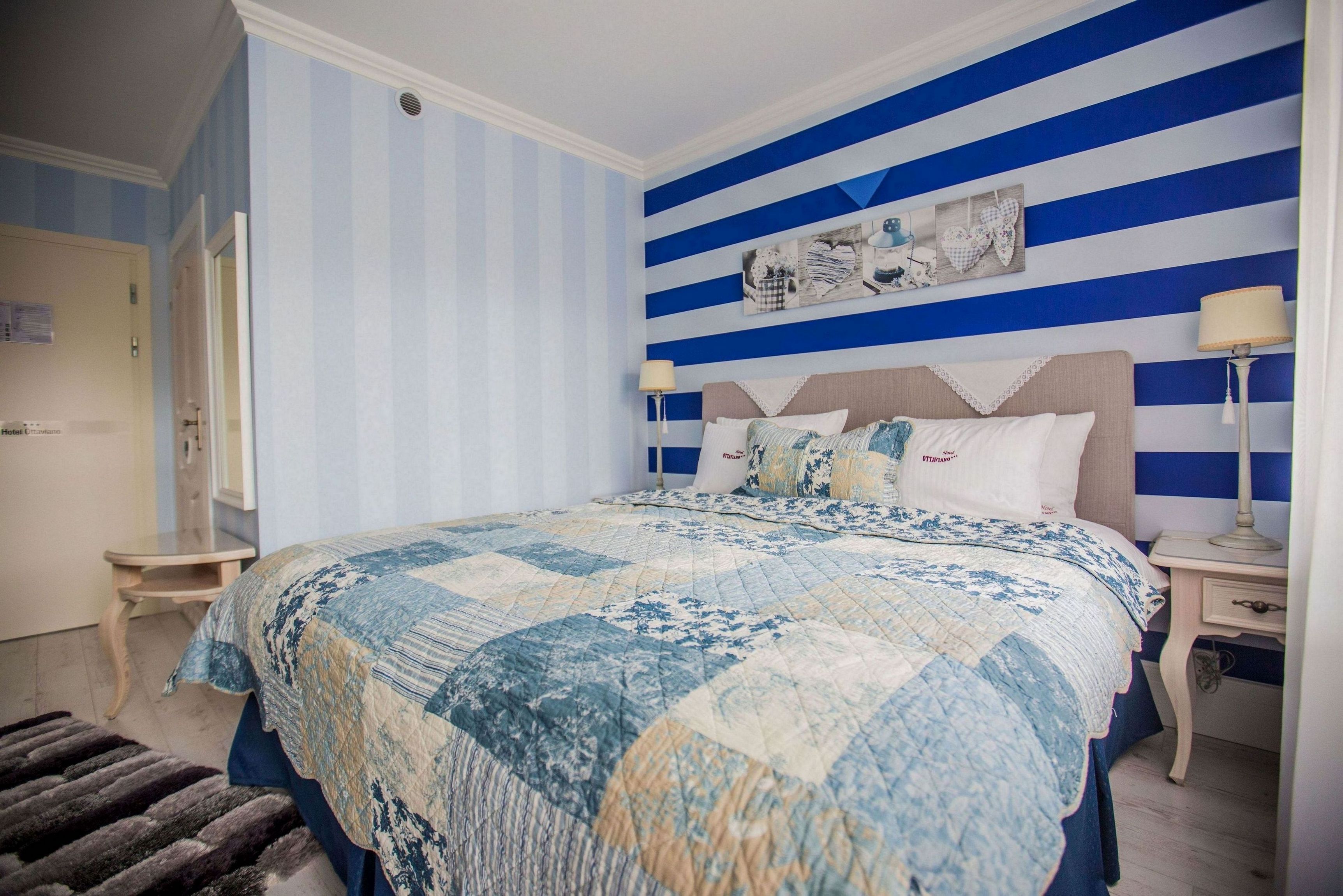 Un dormitorio con cama, paredes a rayas, una mesita de noche y una lámpara.