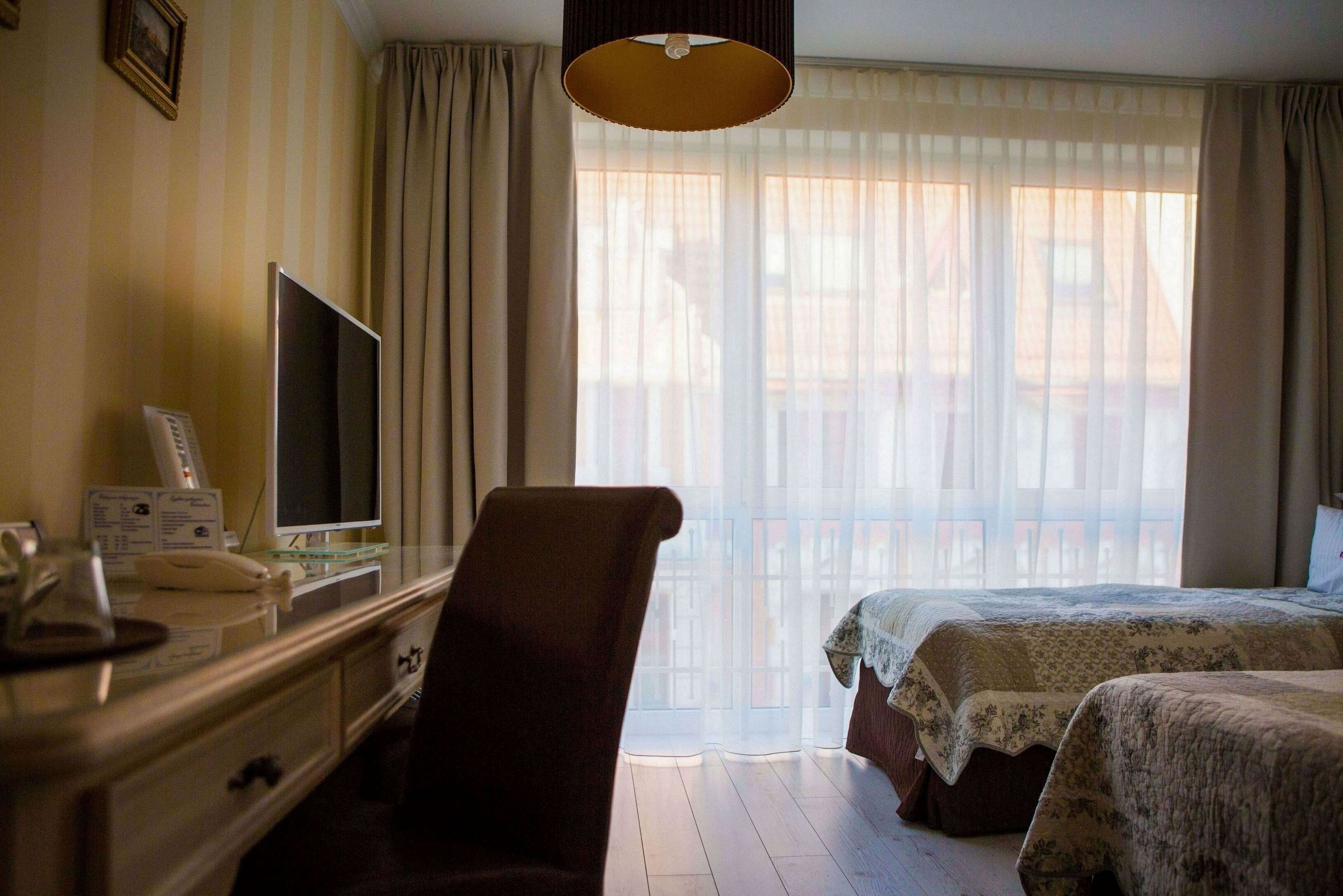 Une chambre d’hôtel avec un lit, une chaise, un bureau avec une télévision et une fenêtre avec des rideaux.