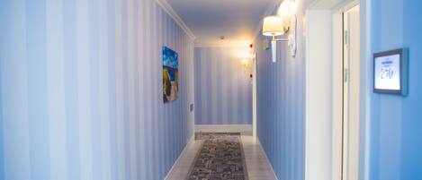 A hallway with striped walls, a patterned carpet, and a door with a number sign.