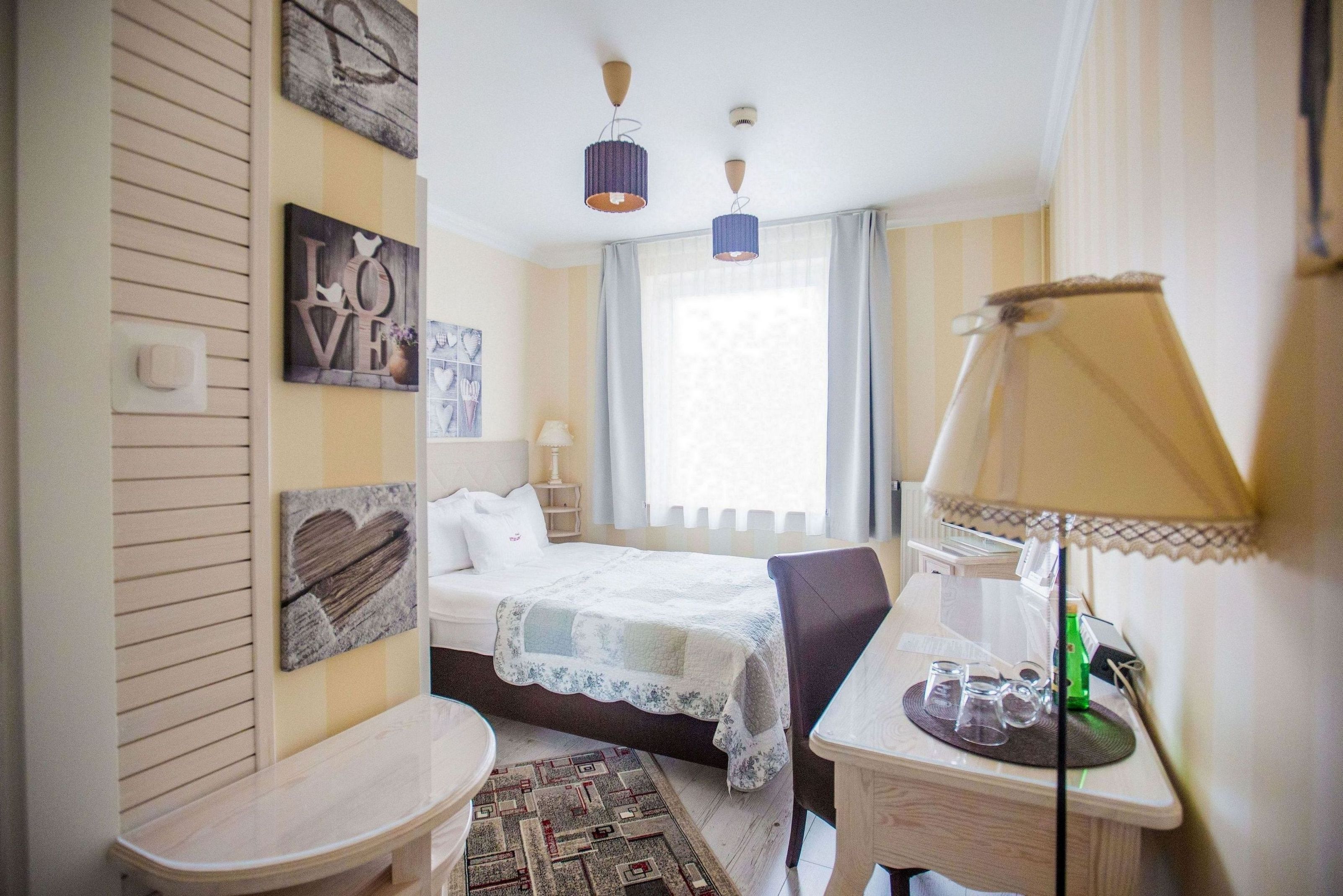 Quarto com cama, mesa de cabeceira, abajur e decorações nas paredes.