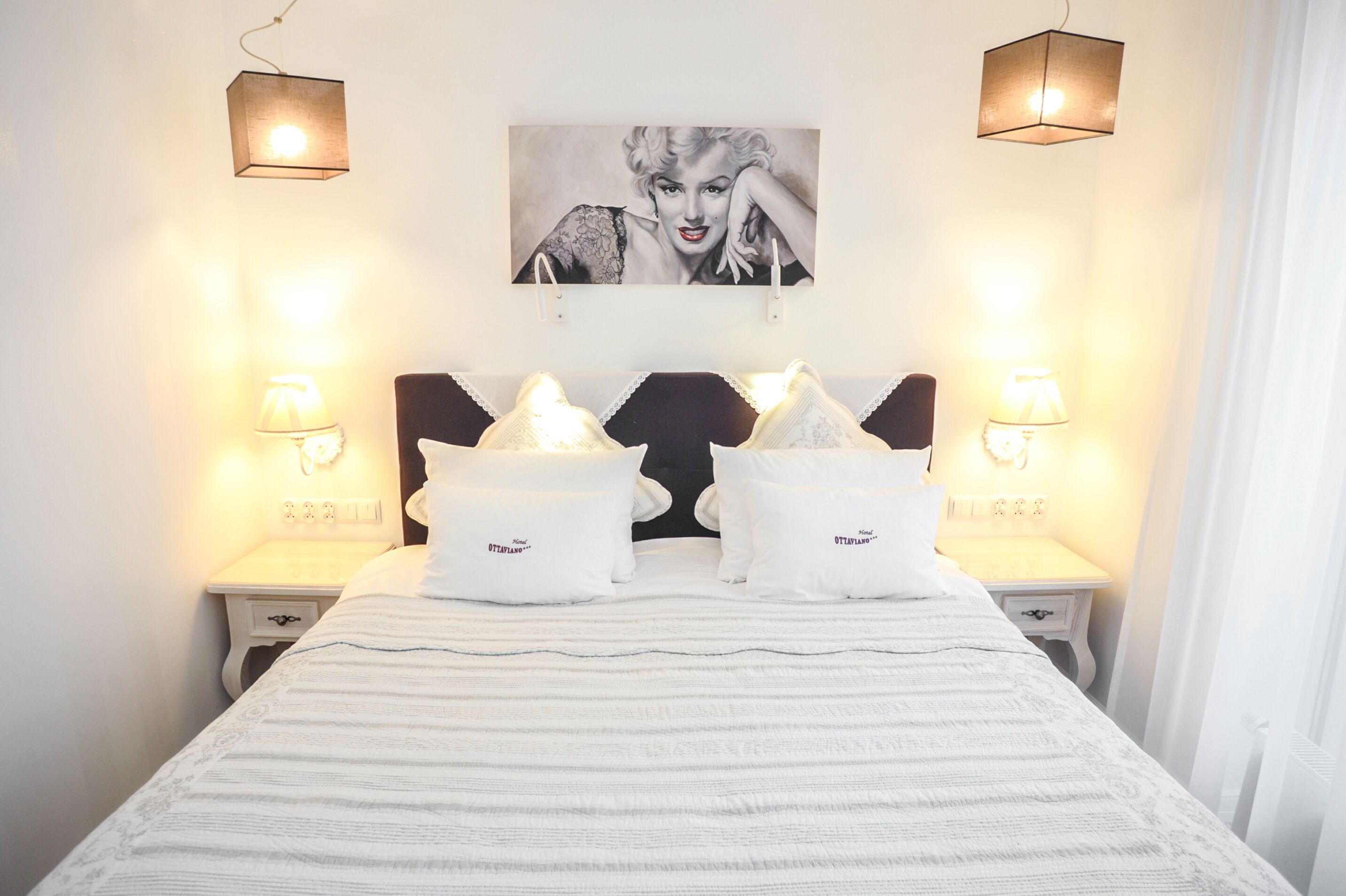 A neatly made bed with white linens, two bedside tables with lamps, and a framed picture on the wall.