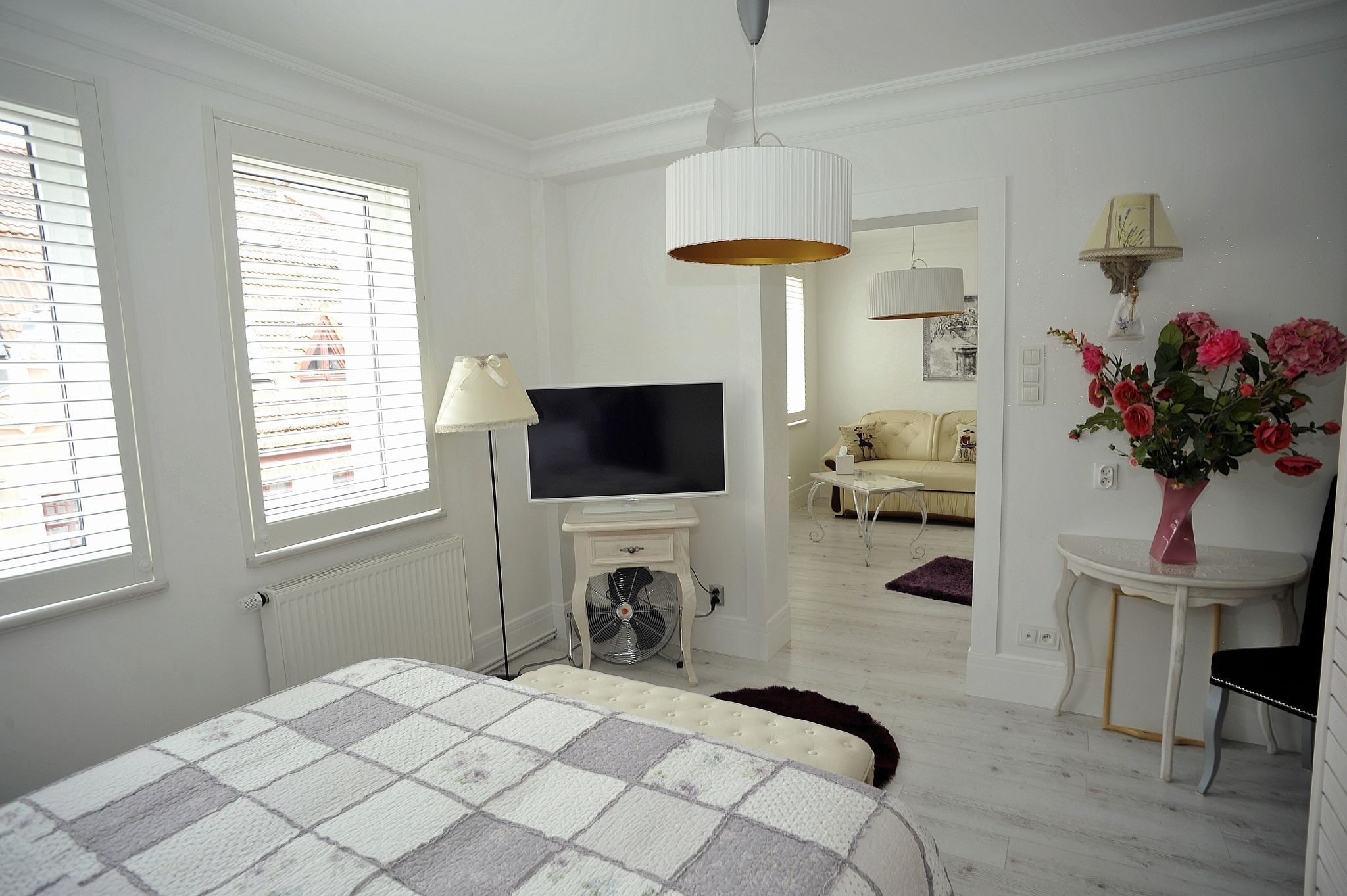 A bedroom with a bed, TV, white walls, and a window.