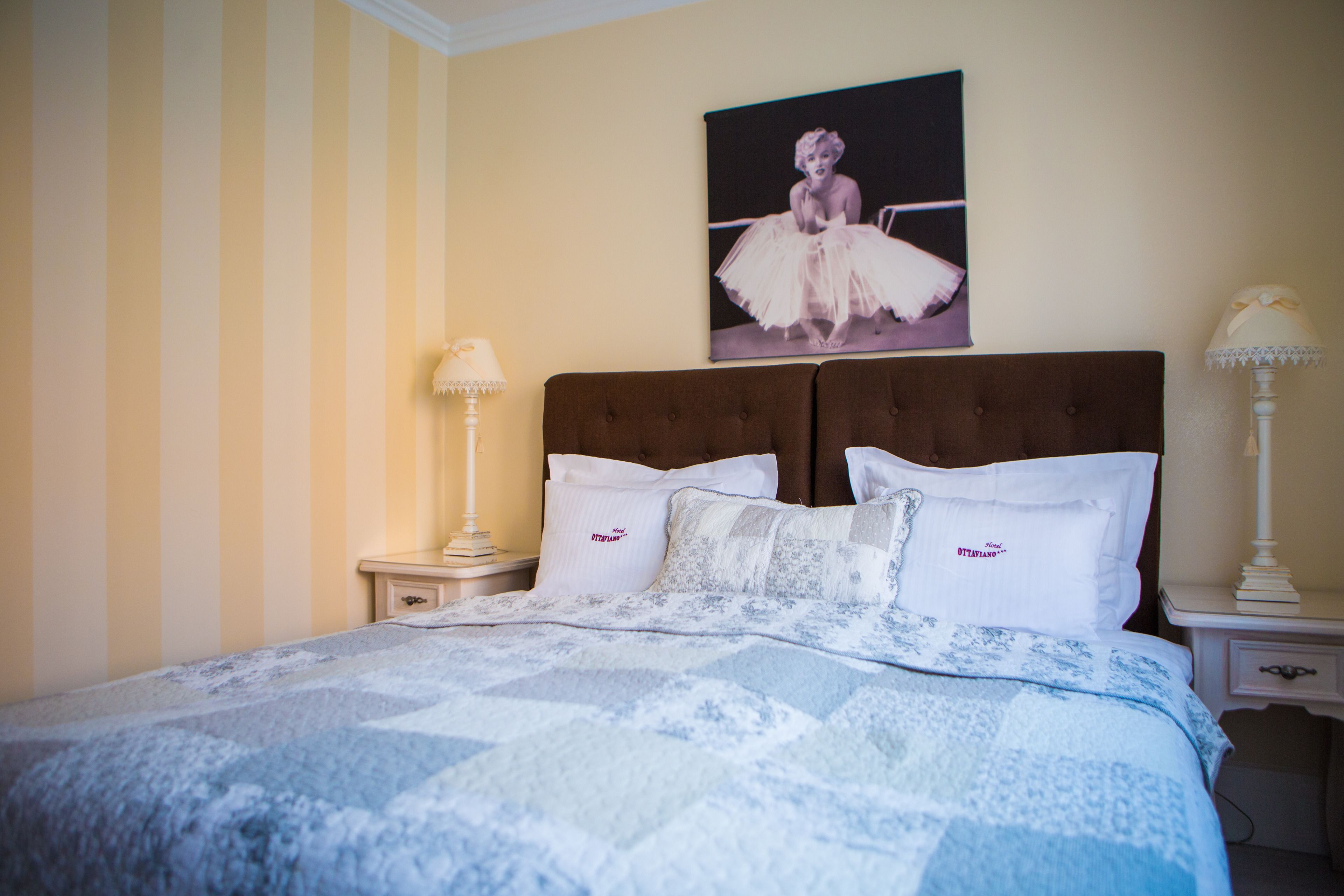 A neatly made bed with a patterned bedspread, two bedside lamps, and a framed picture on the wall.