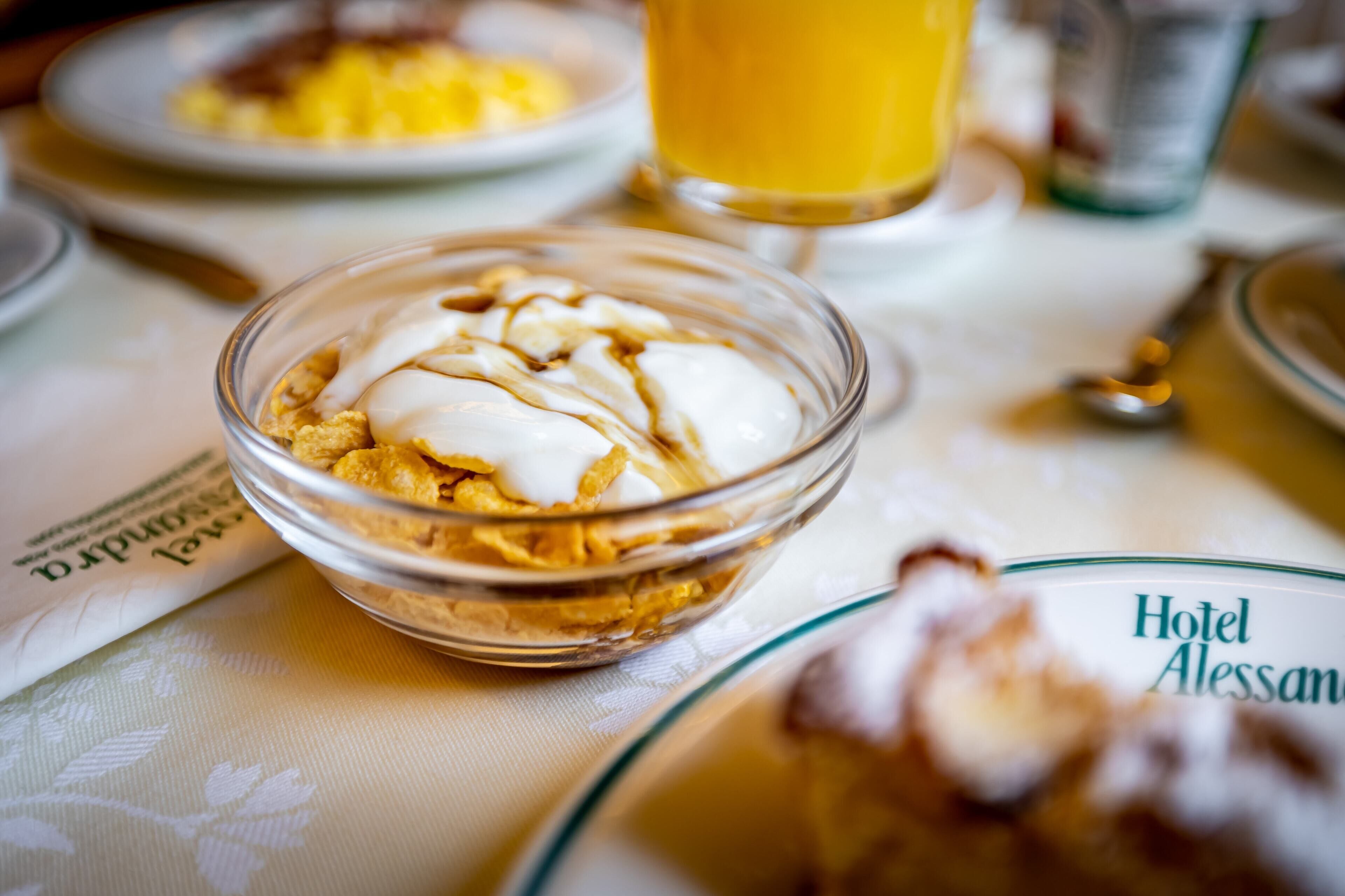 Frühstückstisch mit einer Schüssel Müsli, einem Glas Orangensaft und einem Teller mit einem Hotelnamen.