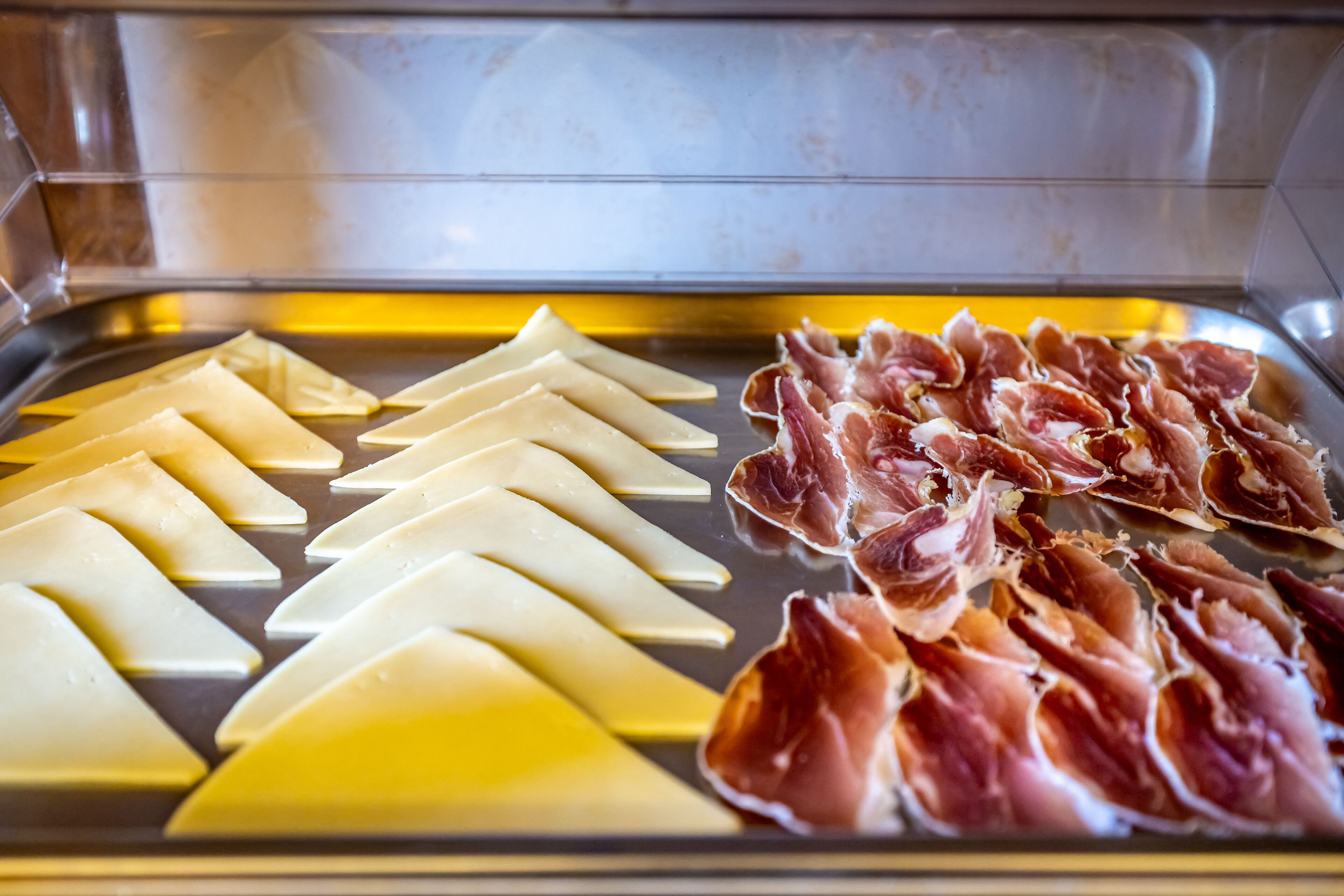 Une sélection de fromages et de charcuteries présentés dans un réfrigérateur.