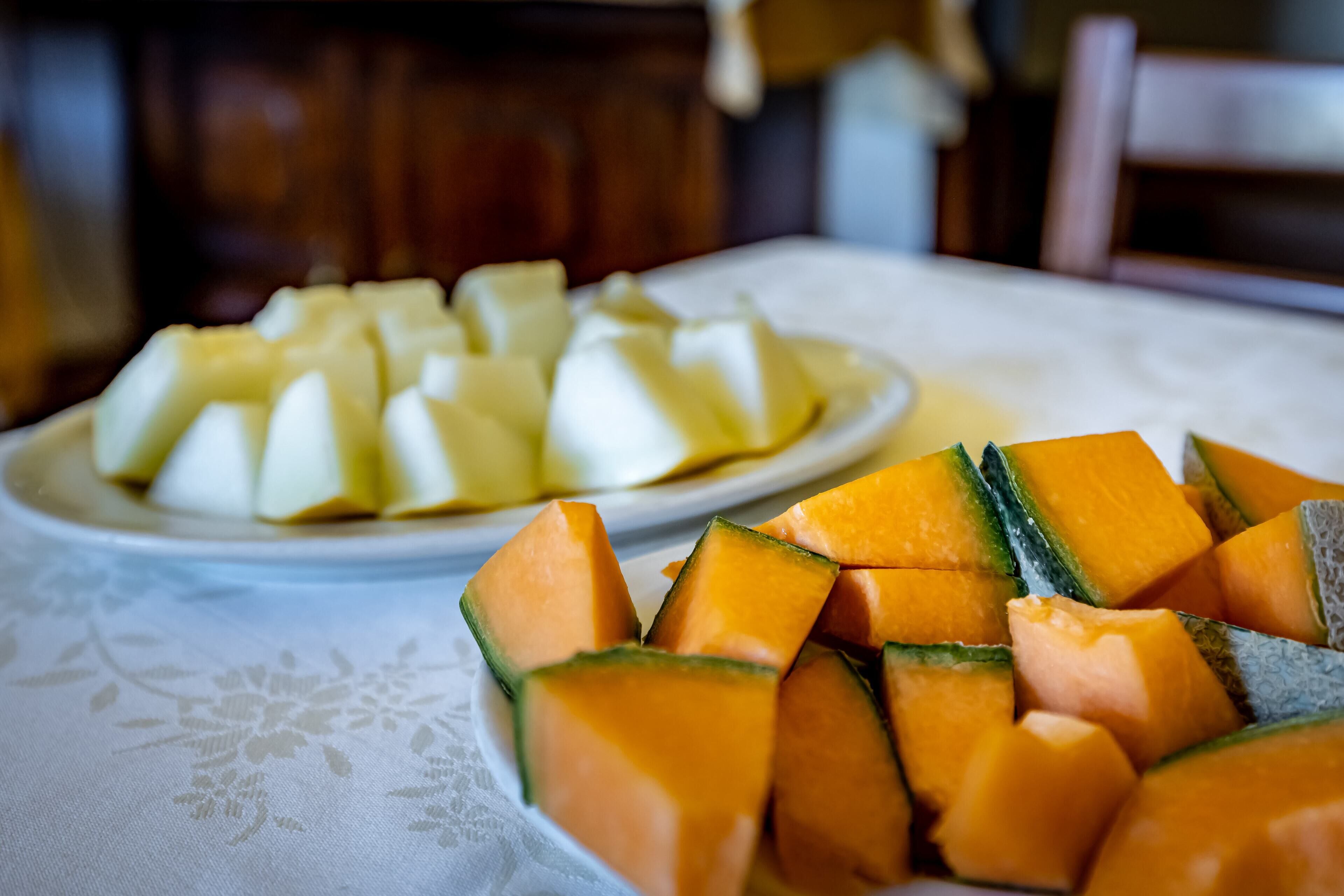 Ein Tisch mit weißer Tischdecke, zwei Fruchtschalen – eine mit Melone, die andere mit Ananasstücken.