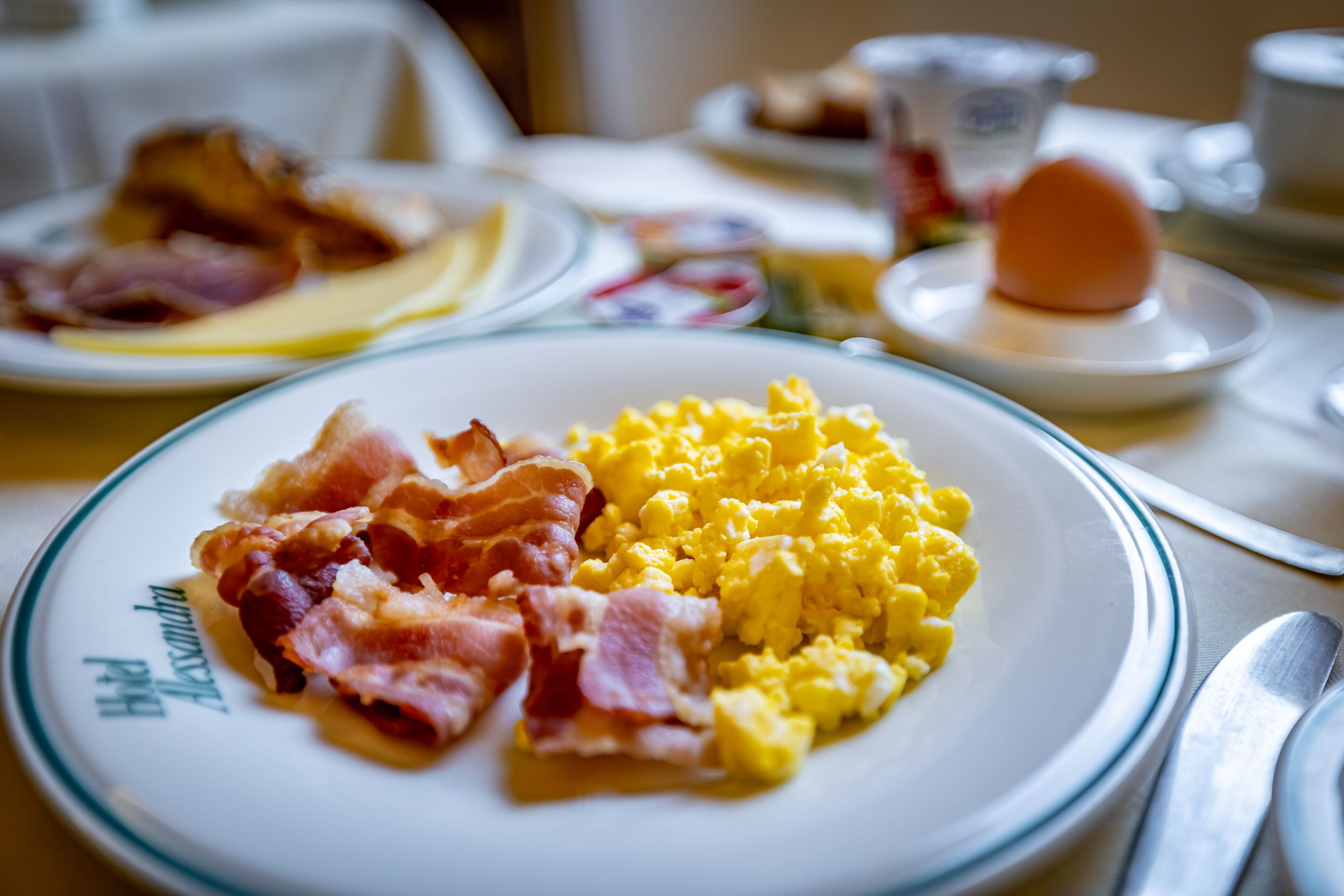 A breakfast plate with scrambled eggs and bacon, a cup of coffee, and a plate with a boiled egg.