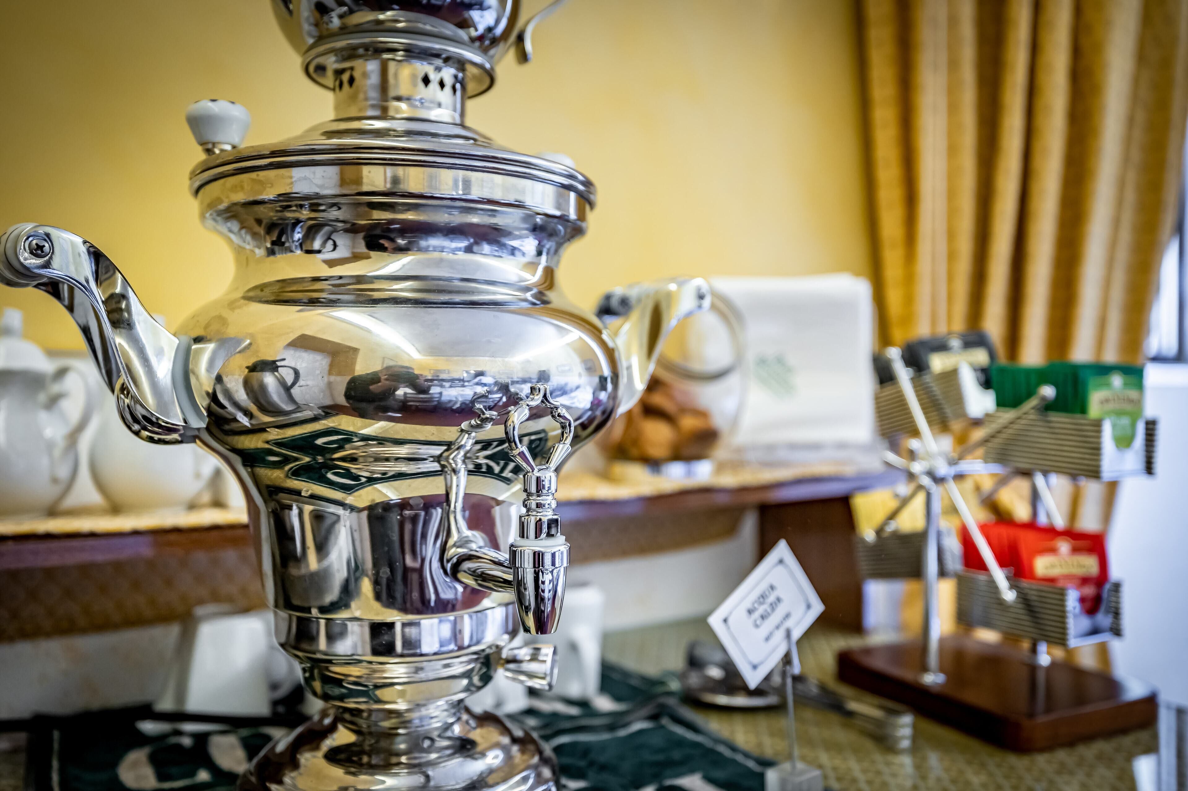 Un samovar traditionnel en argent, doté d’un bec verseur et d’un couvercle, est placé sur une table, accompagné d’une pancarte indiquant qu’il est à vendre.