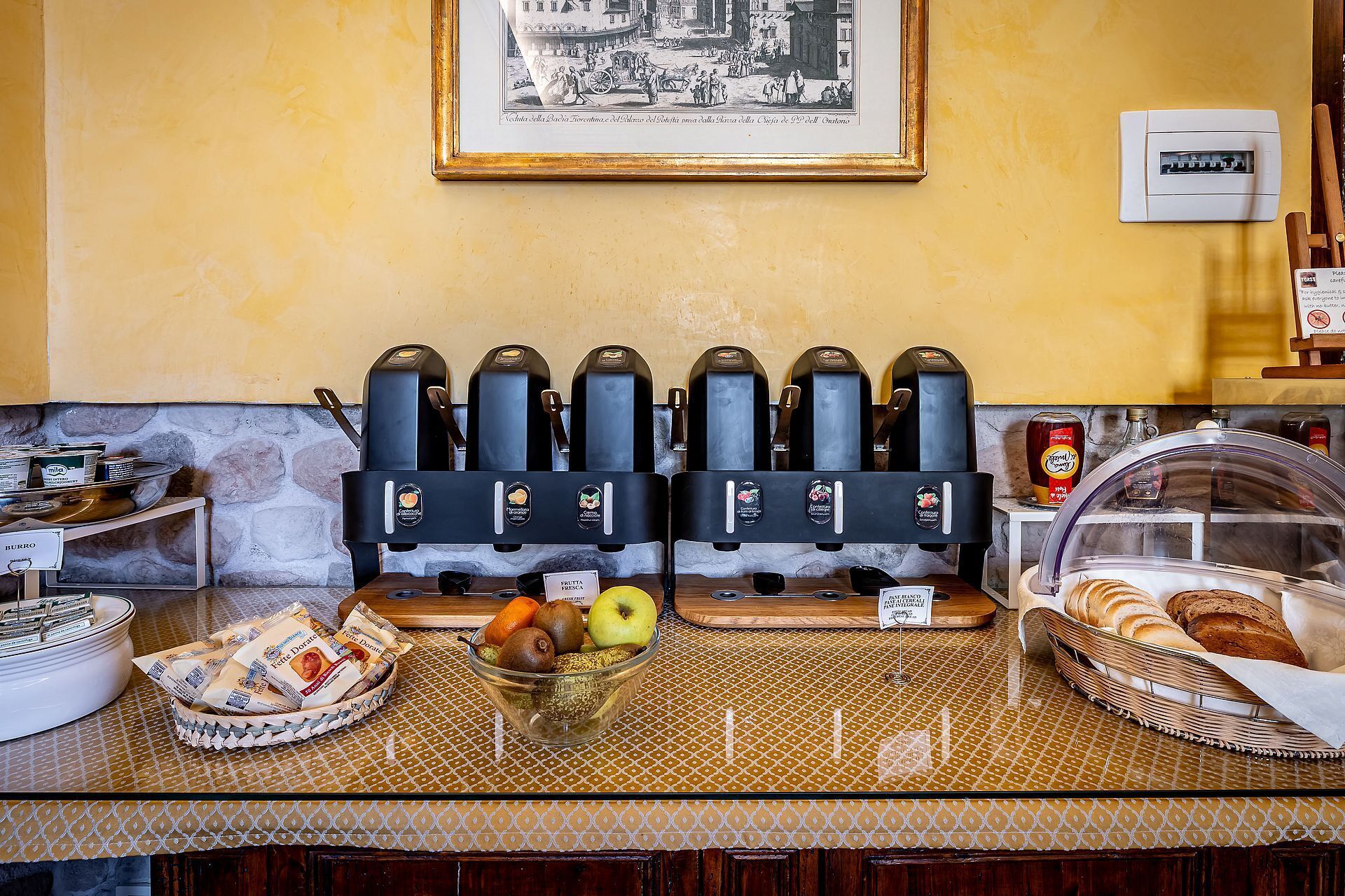 A breakfast bar with coffee machines, a fruit bowl, and a basket of bread.