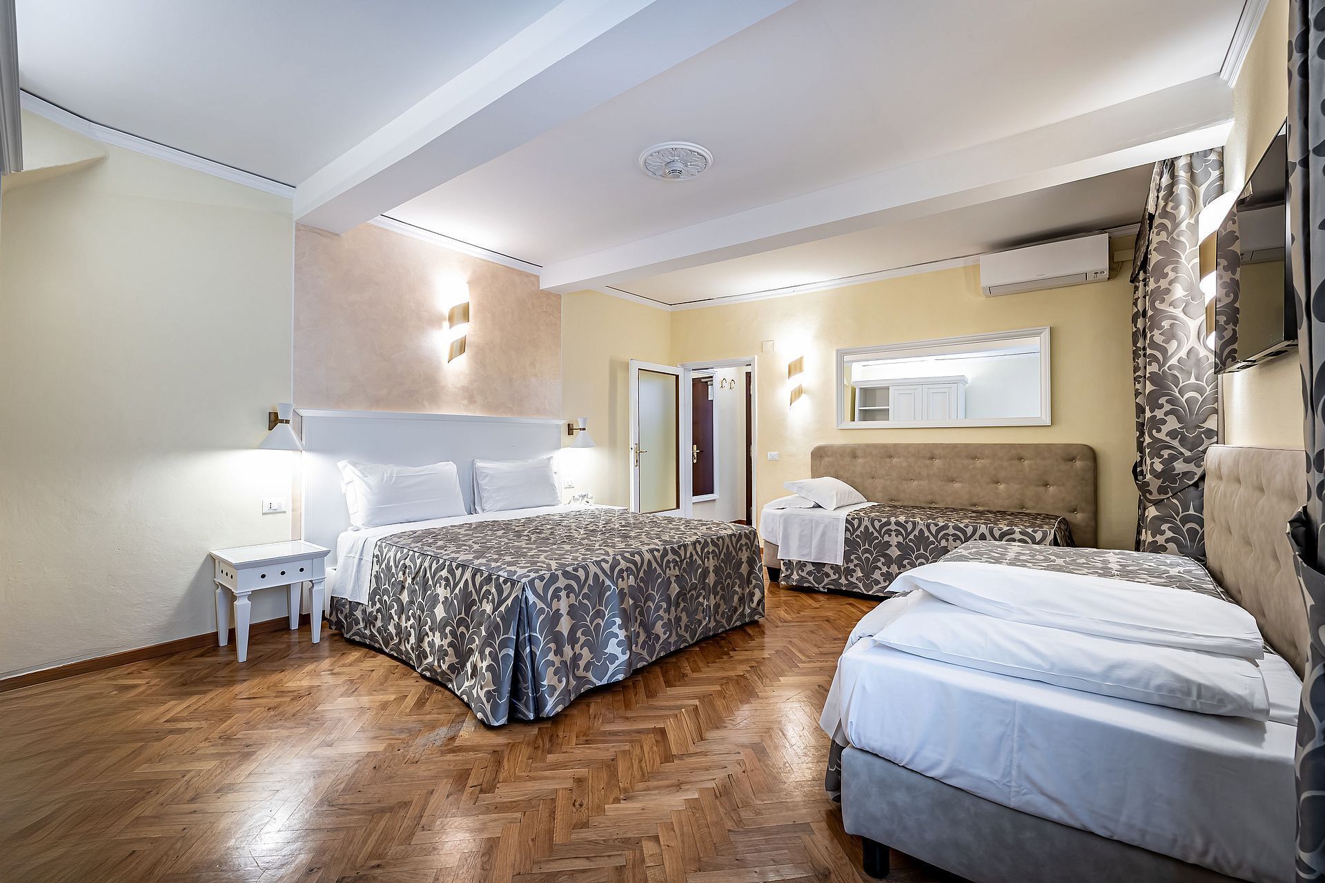 Habitación de hotel con dos camas, suelo de madera en espiga, un espejo grande y un equipo de aire acondicionado.