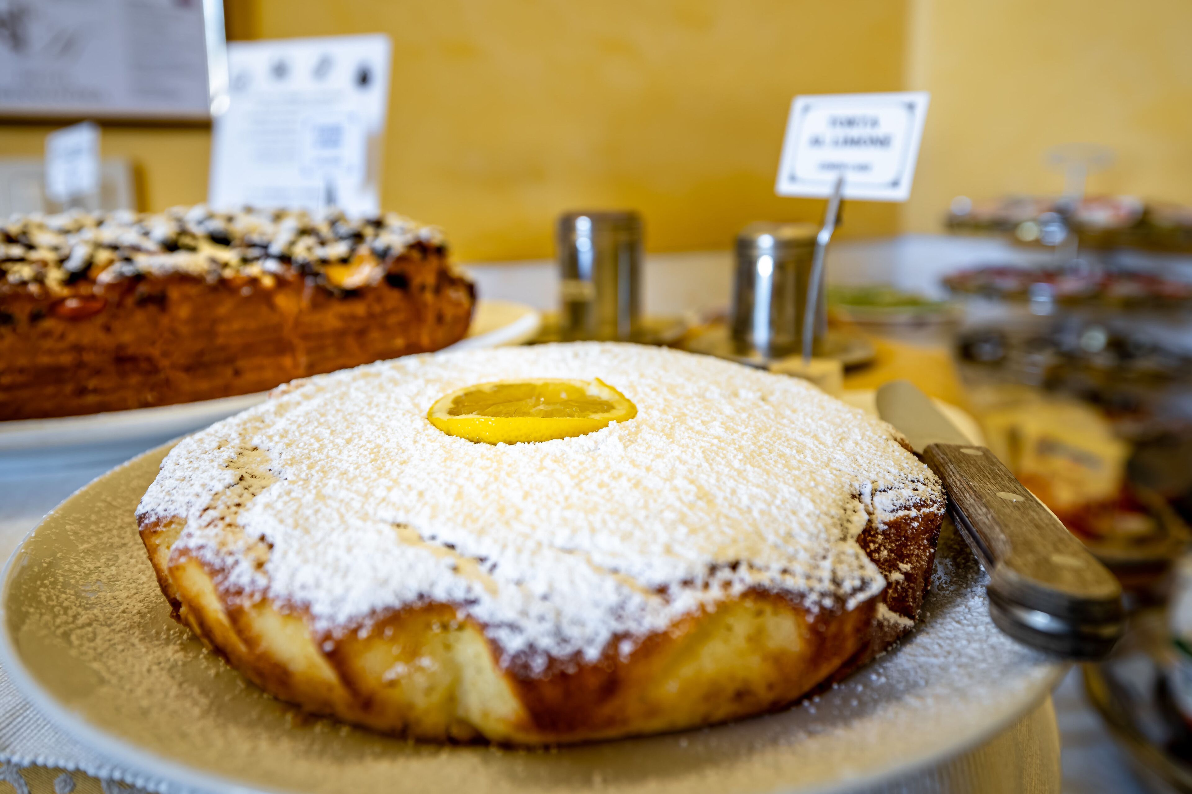 A dessert display with a cake topped with powdered sugar and a slice of lemon.