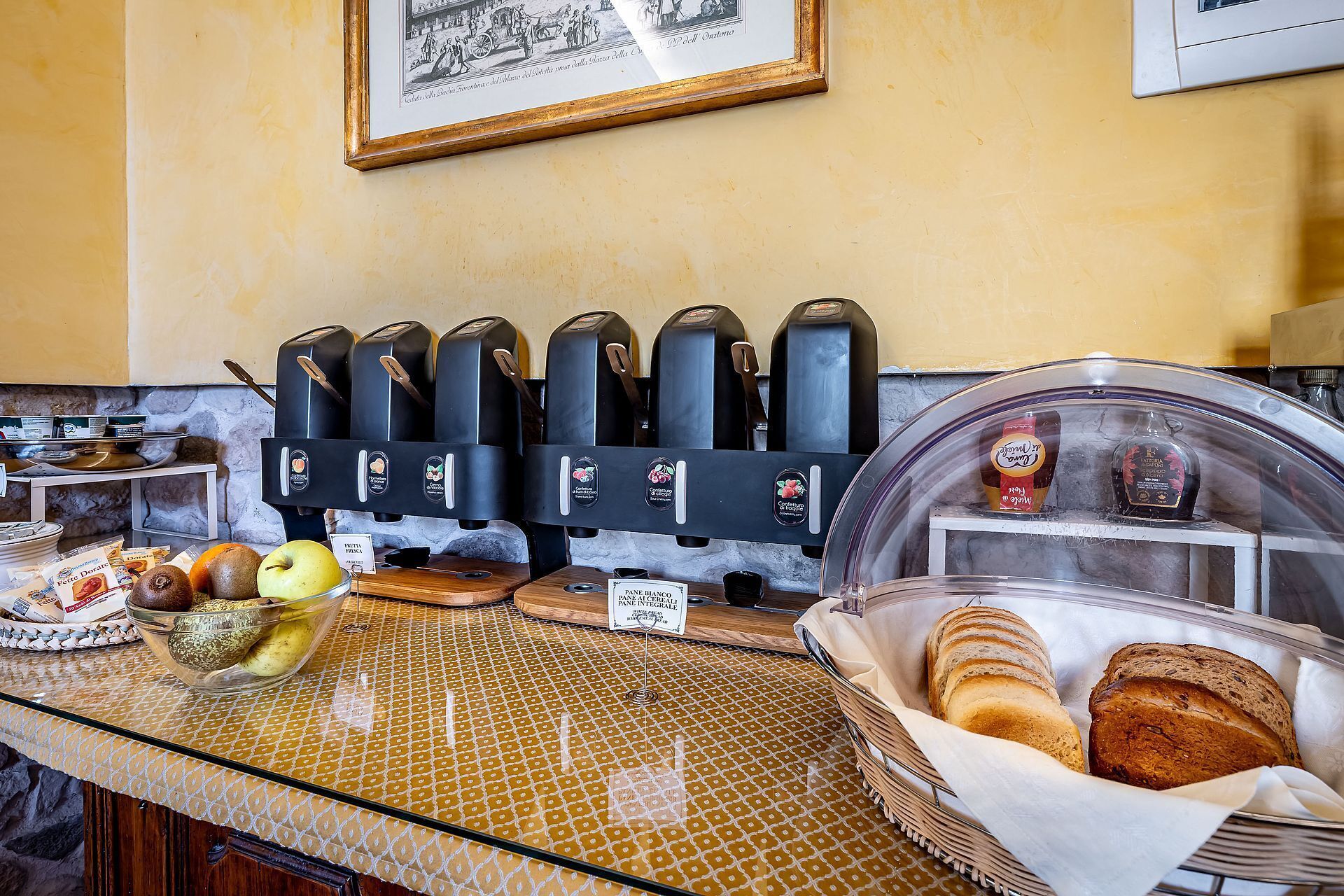 A breakfast bar with coffee machines, a fruit bowl, and bread baskets.