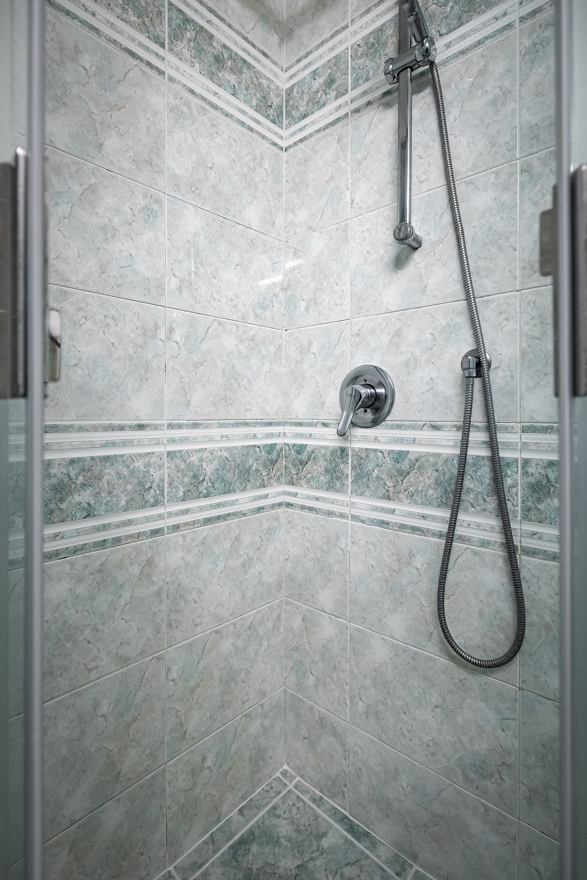 Une douche équipée d’un pommeau de douche à main et d’un robinet mural fixe, installée dans un coin et agrémentée d’un pare-splash en carreaux de marbre.