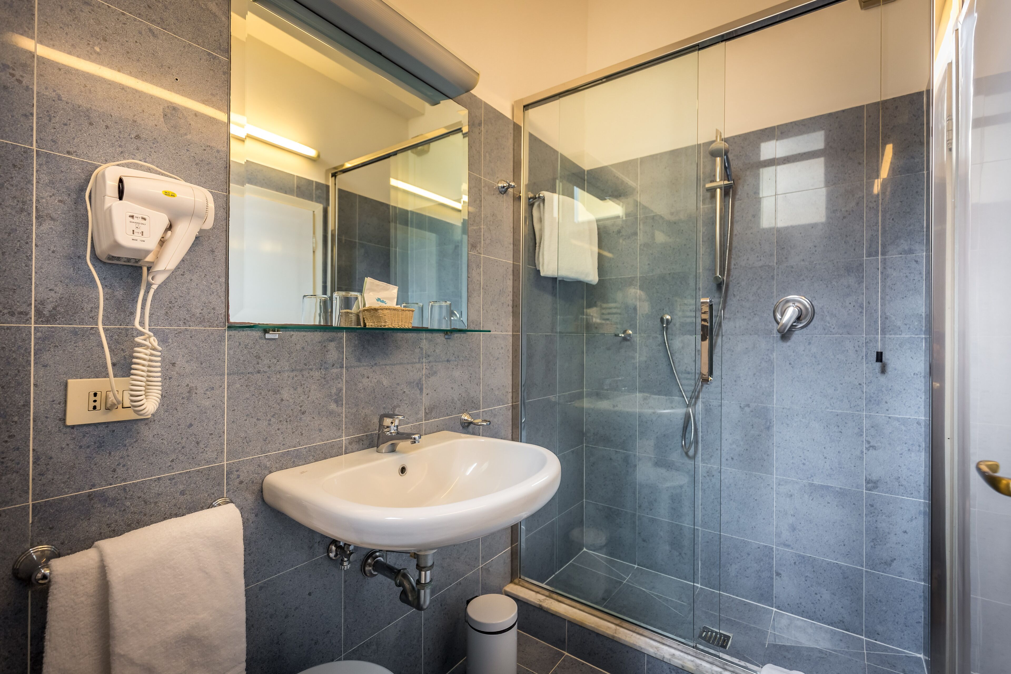 Une salle de bain moderne avec une douche à parois de verre, un lavabo blanc et un sèche-cheveux fixé au mur.