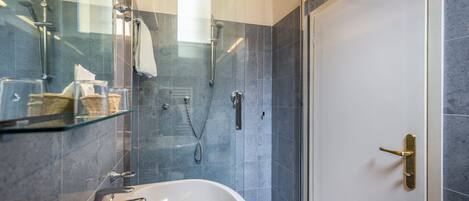 A modern bathroom with a glass shower enclosure, a white sink, and a glass shelf with toiletries.