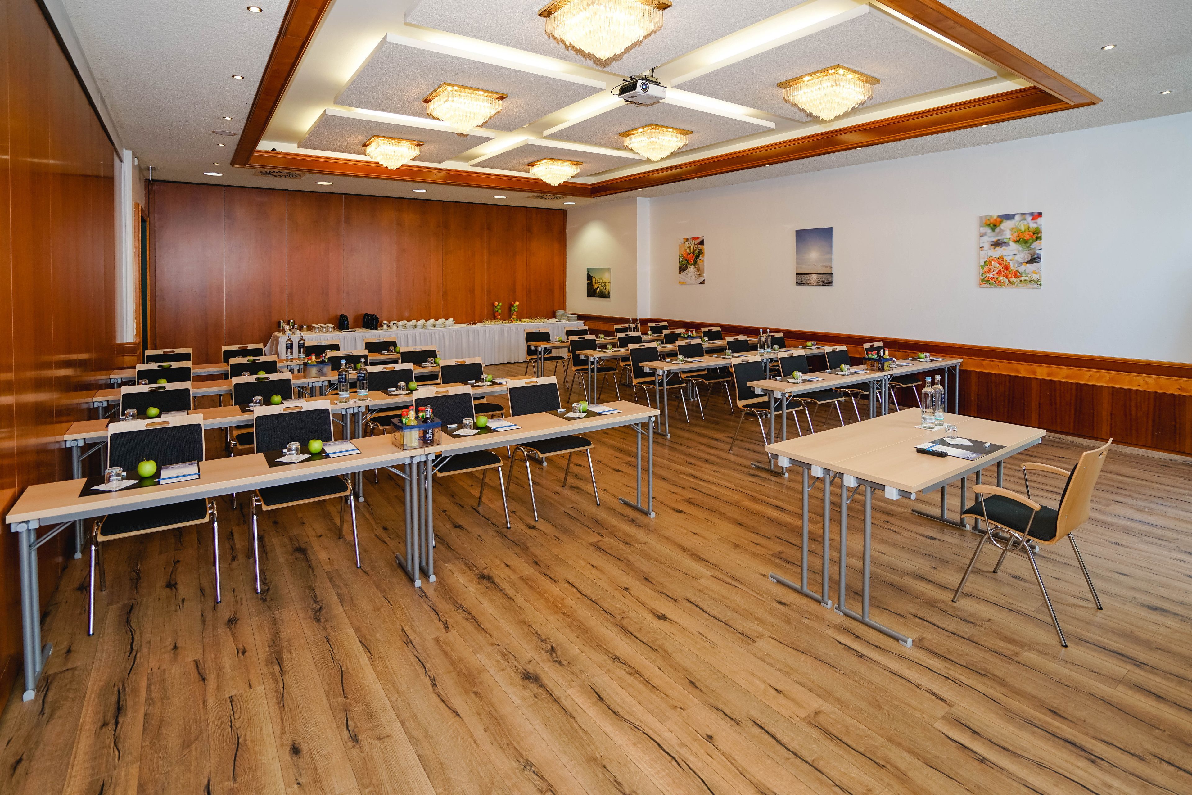 A conference room with multiple tables and chairs, wooden floors, and ceiling lights.