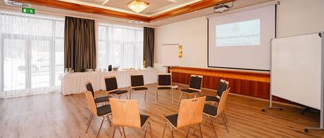 A conference room with a round table, chairs, a projector screen, and a whiteboard.