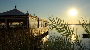 A gazebo with a glass enclosure overlooking a body of water, surrounded by tall grass.
