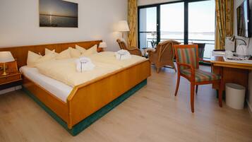 Habitación de hotel con una cama grande, un escritorio, una silla y vista al mar por las ventanas.
