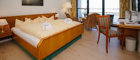 Habitación de hotel con una cama grande, un escritorio, una silla y vista al mar por las ventanas.