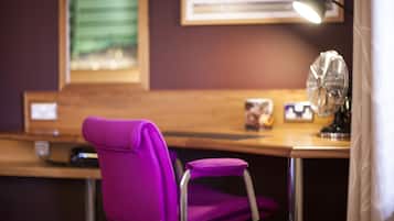 A purple chair and a desk with a lamp and a fan.
