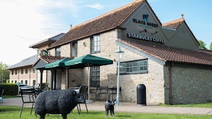 A building with a stone facade and a sign for 'Black Sheep Bar & Restaurant' and 'Starbucks Coffee'. There are outdoor seating areas with chairs and umbrellas. - Lodge at Bristol (Bristol)