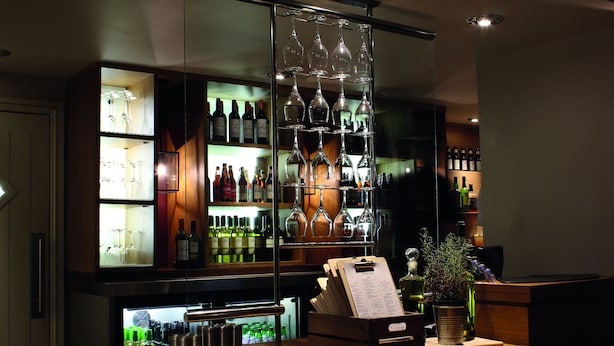A bar area with shelves of wine bottles and glasses, a wooden counter with a menu, and a potted plant. - Lodge at Bristol (Bristol)